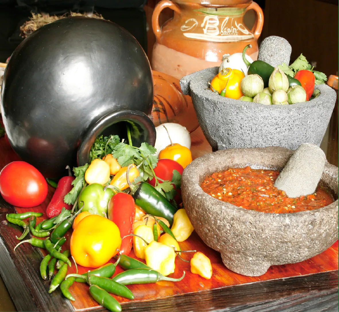 Molcajetes with salsa and fresh chiles beside traditional clay pots
