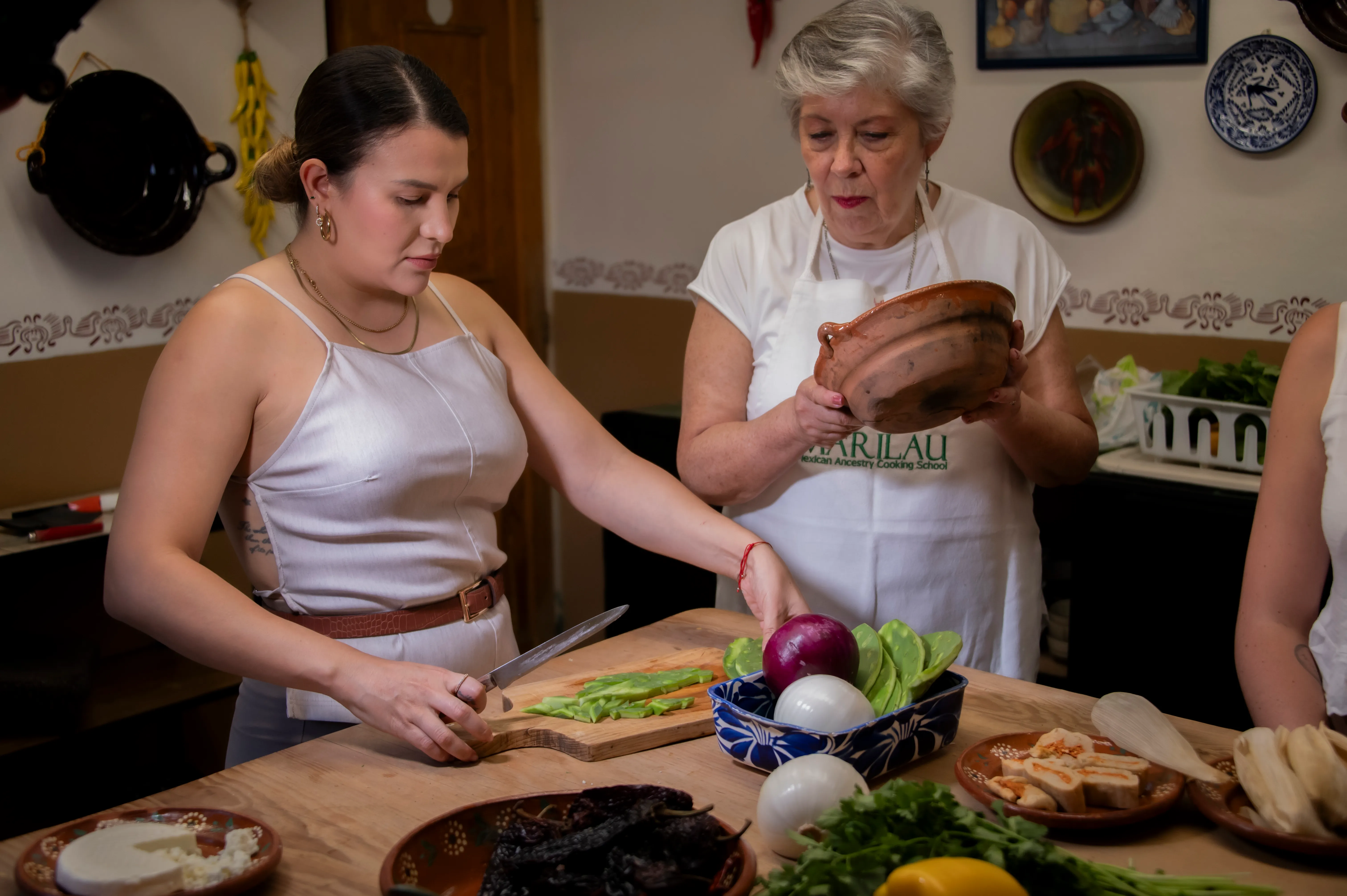 A student slices nopales while Marilau shows a traditional clay pot