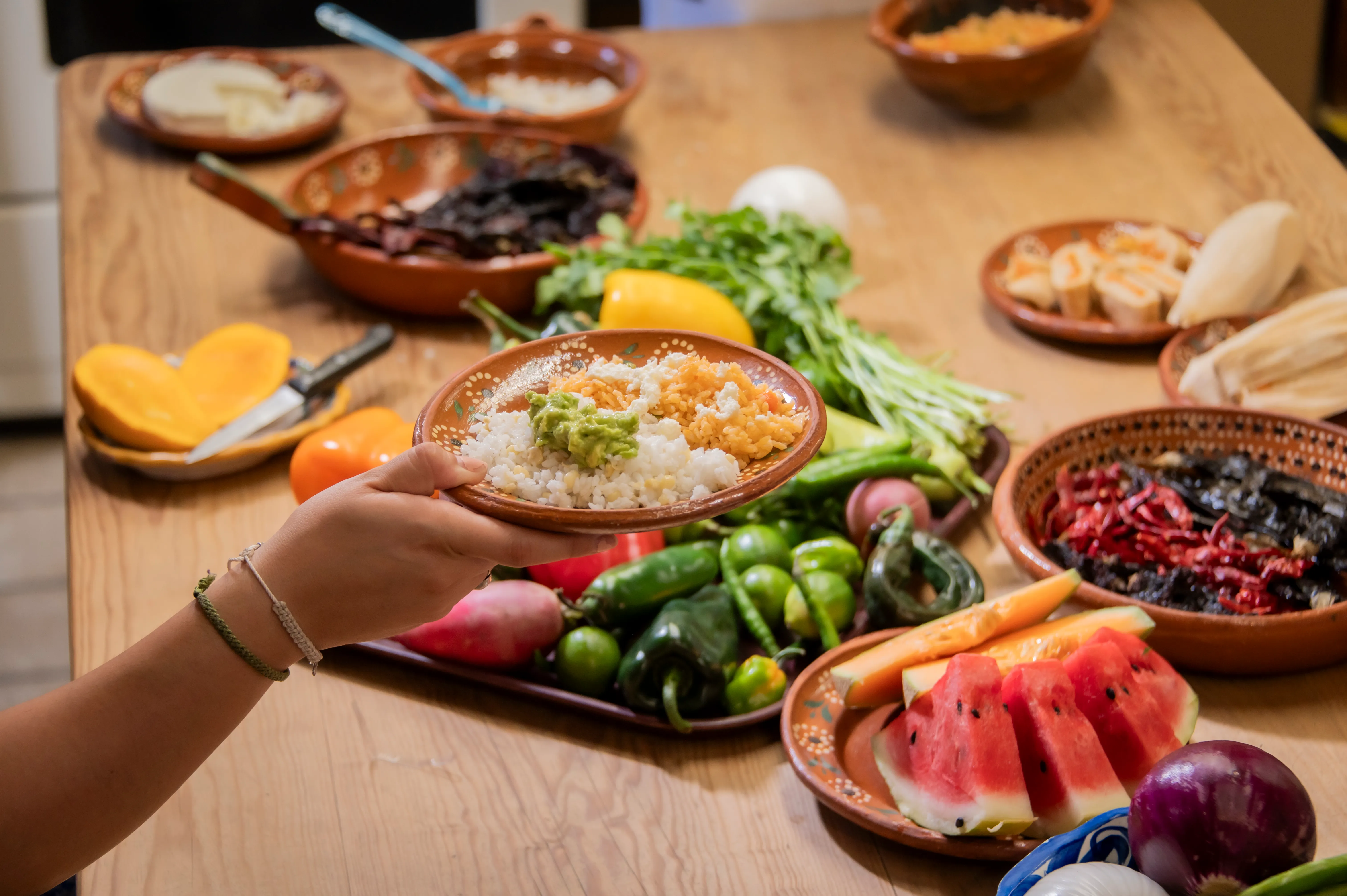 A student holds up her plated dish over a table of fresh Mexican ingredients