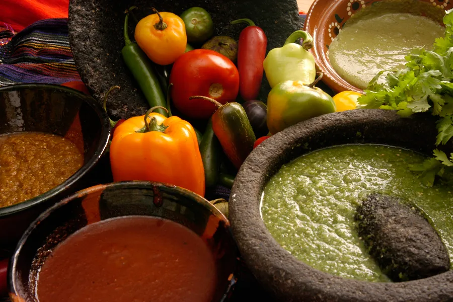 Four salsas in molcajetes and clay bowls surrounded by fresh chiles